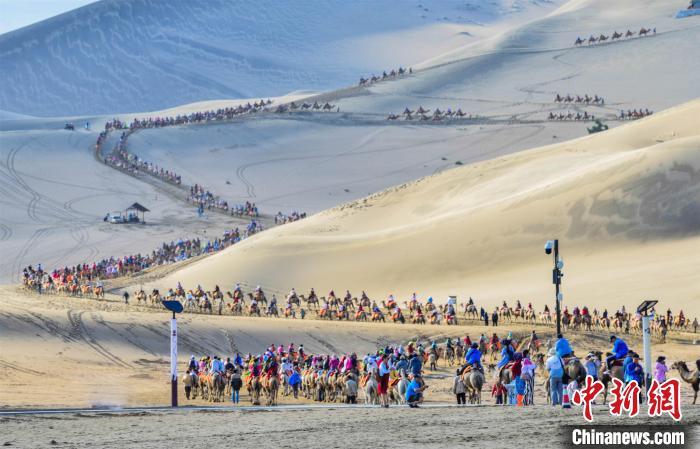 2019年7月18日，中外游客在敦煌鸣沙山月牙泉景区骑骆驼观光游览，形成近2公里长的宛如长龙的观光驼队。王斌银 摄